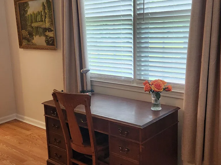 Bedroom workspace nook with hardwood floors, a large window with shutters, and a desk/dresser for study and storage.