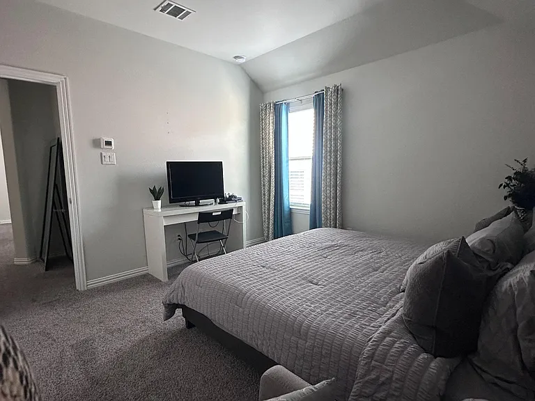 Spacious carpeted bedroom with a large window, closet access, and room for a bed plus a work desk setup.