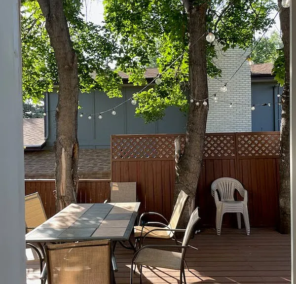 Lights hung above porch table for summer meals, BBQ to the left, additional sitting area to the left, hottub and fenced back yard to the left with the spacious greenbelt beyond.