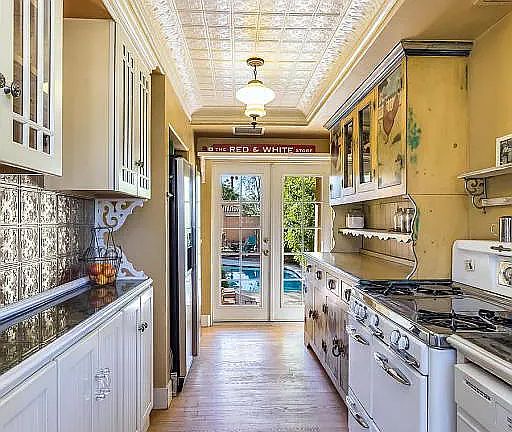 Galley-style kitchen with granite countertops, farm sink, statement cabinetry, and and French doors leading to the back yard and pool area.