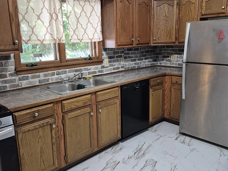 Kitchen view from back door, showing refrigerator, dishwasher, and sink, and new marble-look laminate tile flooring.