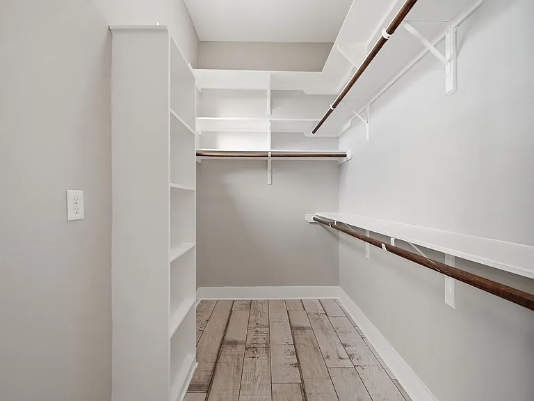 One of two spacious walk-in closets designed for elevated storage and organization. Featuring light gray walls, warm wood flooring, and extensive shelving and hanging space, this bright, well-lit closet blends functionality with modern style.
