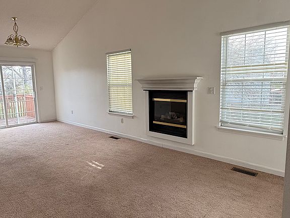 This versatile living room is spacious and bright, featuring large windows, cozy carpeting, and a fireplace. With ample room for both a dining area and a TV setup, the space is perfect for relaxation and entertainment. The ceiling fan adds extra comfort