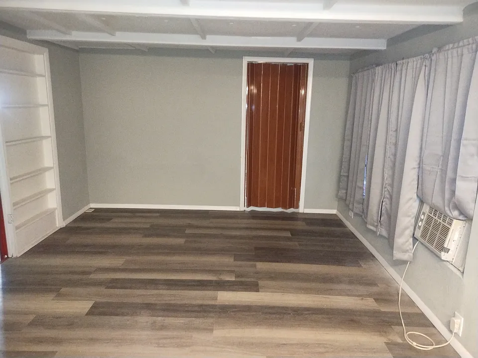 Upstairs living room with new laminate flooring, a built-in shelf to the left and a large window to the right with new curtains and an AC window unit.