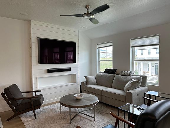 Living room furnished with ceiling fan and blinds.