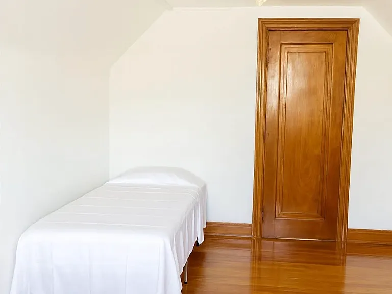 View from the opposite side showing a bedroom furnished with a bed frame, mattress, and bookshelf, offering a comfortable and practical living space.