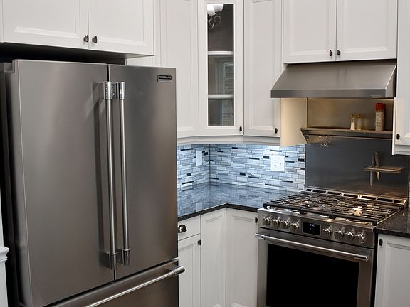 View of refrigerator, gas range, hood and cabinets.