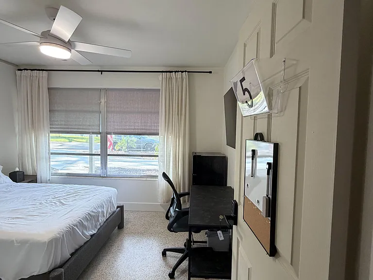 Private bedroom with a comfortable bed, work desk, and a large window dressed with curtains and shades for light control.