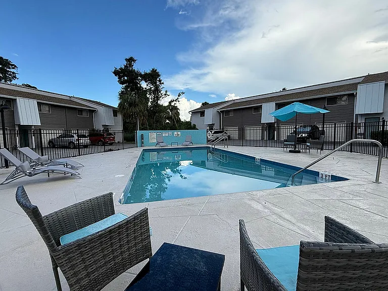 Inviting apartment outdoor area with a sparkling pool, comfortable lounge chairs, and vibrant blue umbrella, perfect for relaxing.