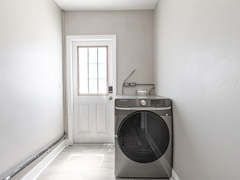 Dedicated laundry area with a full-size washer/dryer and durable tile flooring, conveniently located by an exterior door.