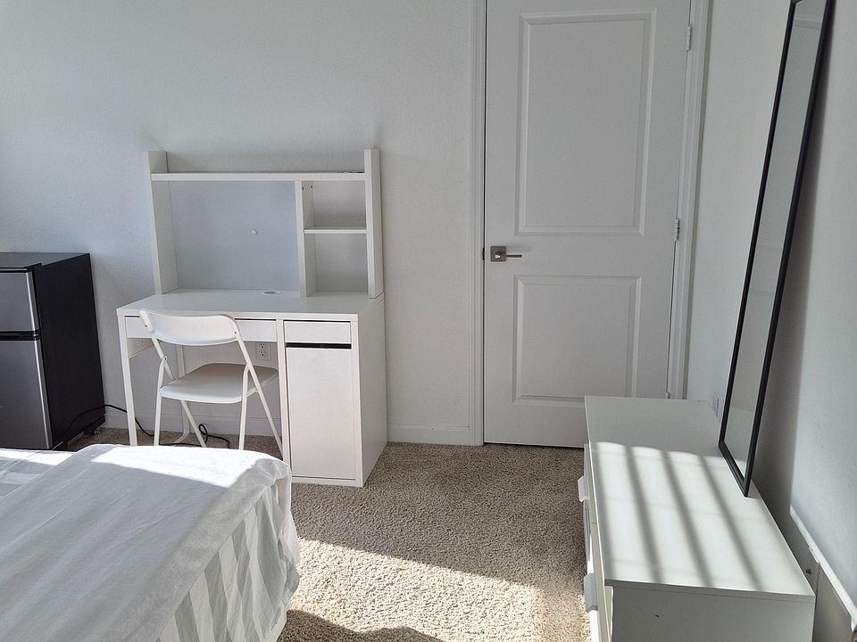 Bedroom features a dedicated desk nook, mirrored dresser, and plush carpet with space for a mini-fridge.
