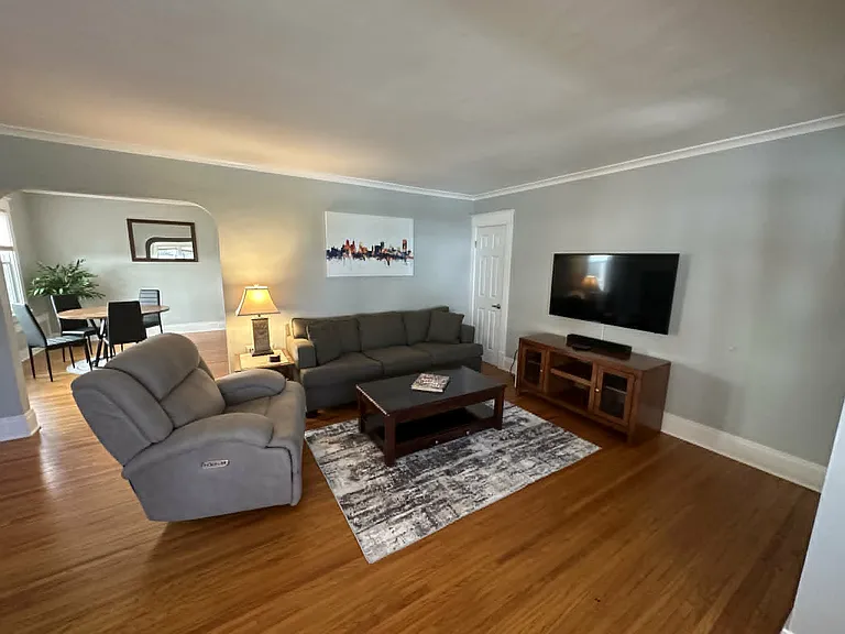 Spacious, fully furnished living room featuring hardwood floors, comfortable seating, and a large Smart TV.