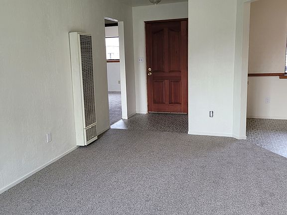 Living Room looking front door and toward doorway to bedroom hall. Also wall furnace