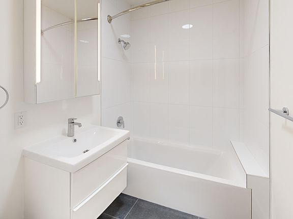 Bathroom featuring a bathtub, sleek sink with drawers, and a mirrored cabinet with LED lighting