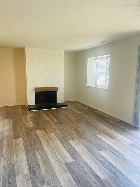 Spacious Living Room with wood flooring and a white brick fireplace to accent.