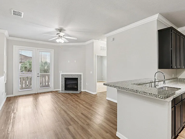 Chic open-concept living space featuring sleek hardwood floors, a contemporary granite kitchen, and a cozy fireplace with elegant French doors opening to a scenic view.