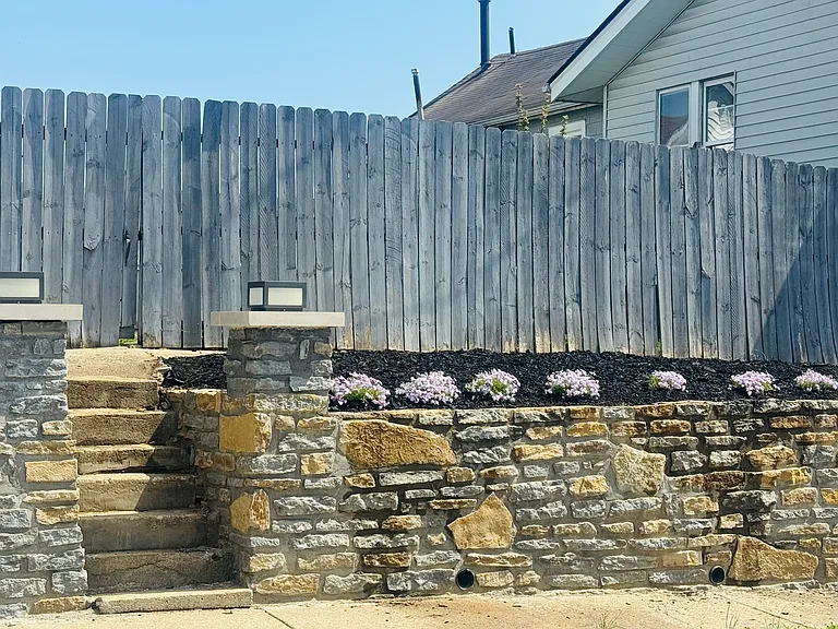 this beautiful stone wall was added in 2025 to enhance the corner lot. The owner added pillars and outdoor lighting incorporated into the retaining wall.