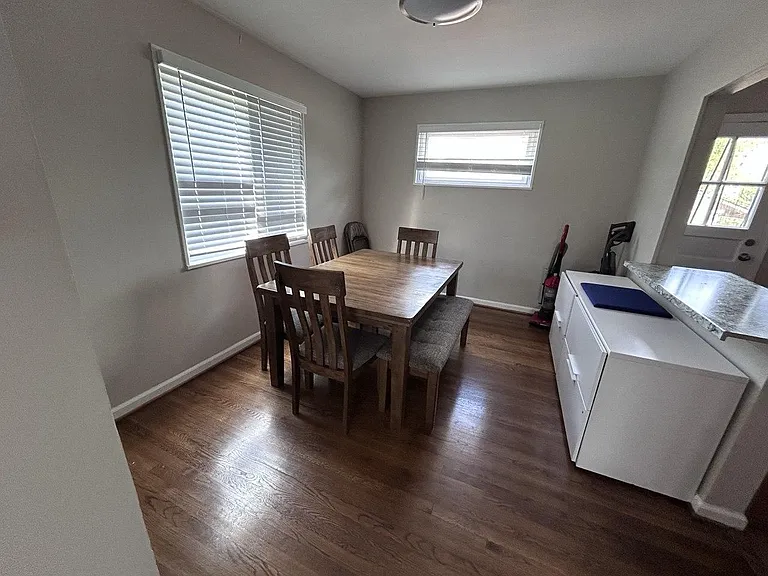 Dining area with a table seating four, durable wood-look floors, and two windows for natural light near the kitchen pass-thro