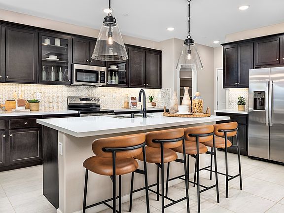 A modern and stylish kitchen with dark cabinets, a white countertop, and pendant lights illuminating