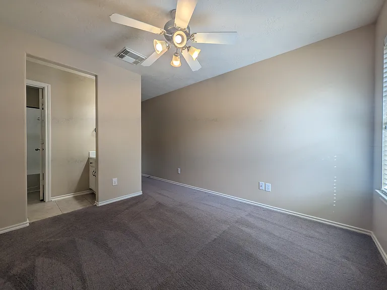 Bright bedroom with plush carpeting and a ceiling fan, featuring direct en-suite access to a dedicated sink and vanity station.