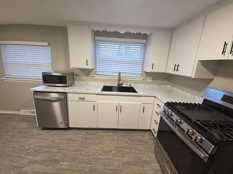 Bright kitchen with updated countertops, white cabinetry, stainless refrigerator and range, and dishwasher.