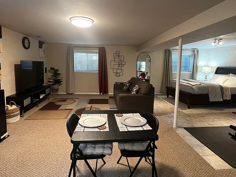 Open-plan private basement suite with queen bed, living area, workspace, and kitchenette.