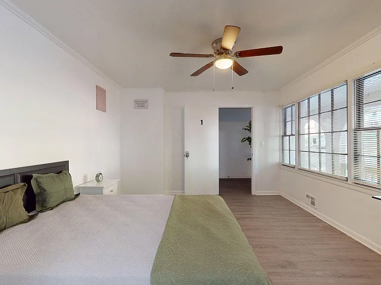 Spacious bedroom with a large window wall, ceiling fan light, and room for a desk or seating area.
