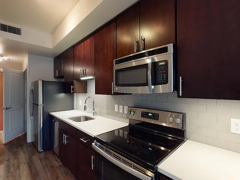 Apartment kitchen with stainless steel appliances, quartz countertops and wood-style flooring.