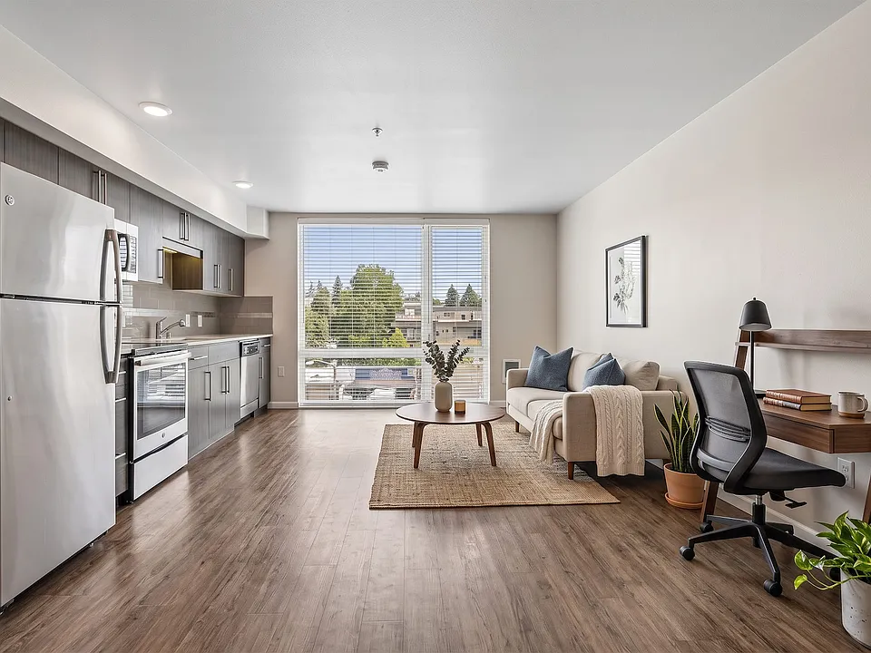 Open living layout at Ludwig Apartments in Seattle featuring a streamlined kitchen, seating area, and ample natural light.