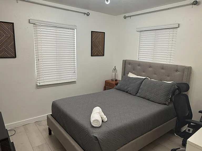 Furnished bedroom with a queen bed, two windows with blinds, and durable tile flooring for easy upkeep.