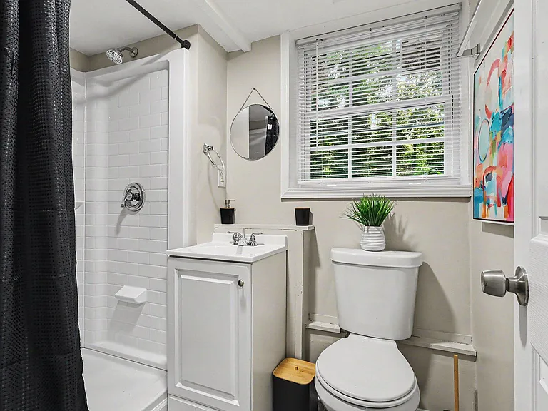 Efficient full bath with tub/shower combo, vanity sink, and a window with blinds for ventilation and natural light.