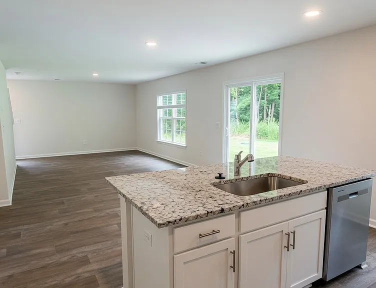 Stainless dishwasher is built-in on the side. Open sightlines continue into the living area and backyard beyond.
