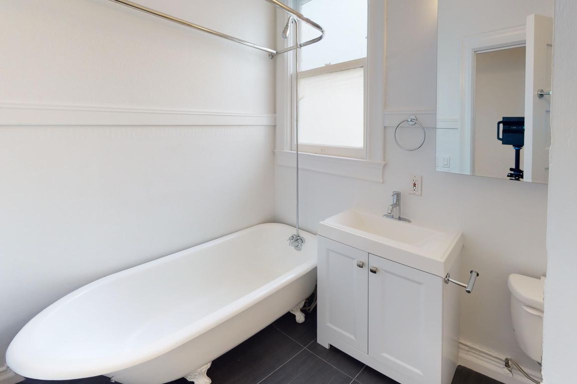 Bathroom featuring a clawfoot tub, sleek sink cabinet, mirror, natural light streams in