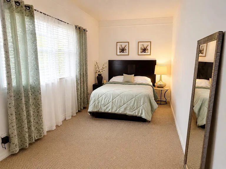 Well-sized bedroom with a full bed, nightstand lighting, and a large window with curtains for privacy and natural light.
