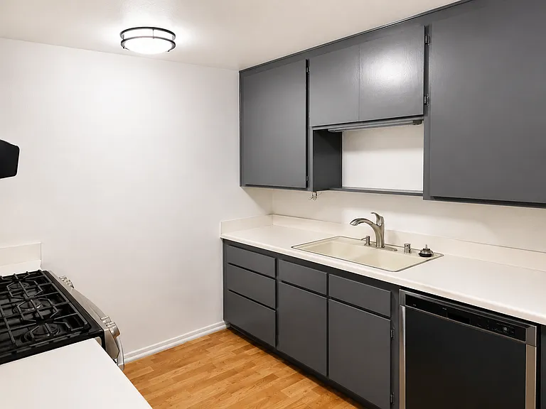 Clean galley-style kitchen with gray cabinetry, light countertops, wood-look flooring, and included appliances.