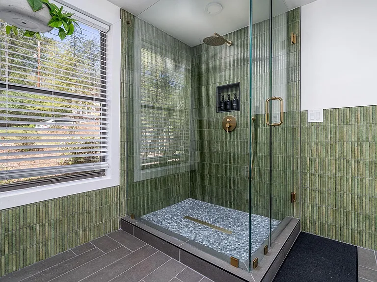 Spa-style walk-in shower with frameless glass, rainfall showerhead, built-in niche shelving, and a large window.