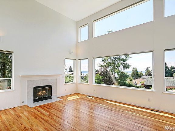 Sunny two story living room with a wall of westerly facing windows.  Gas fire place and just refinished hardwood floors.  Window coverings are included.