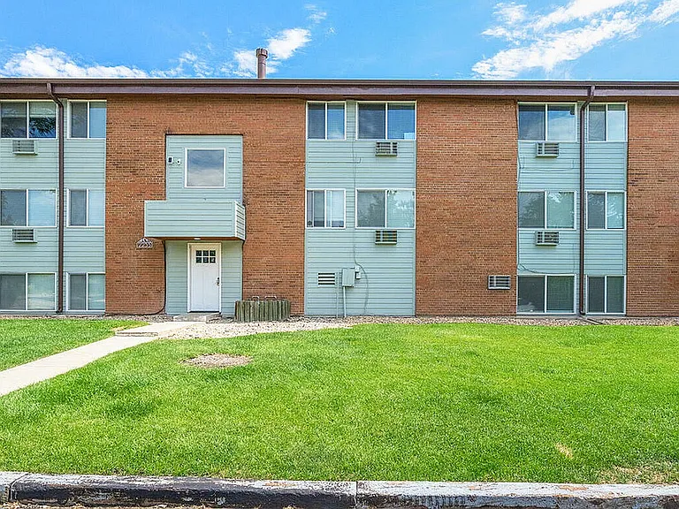 Charming brick apartment building with modern accents, surrounded by lush green lawn under a clear blue sky.