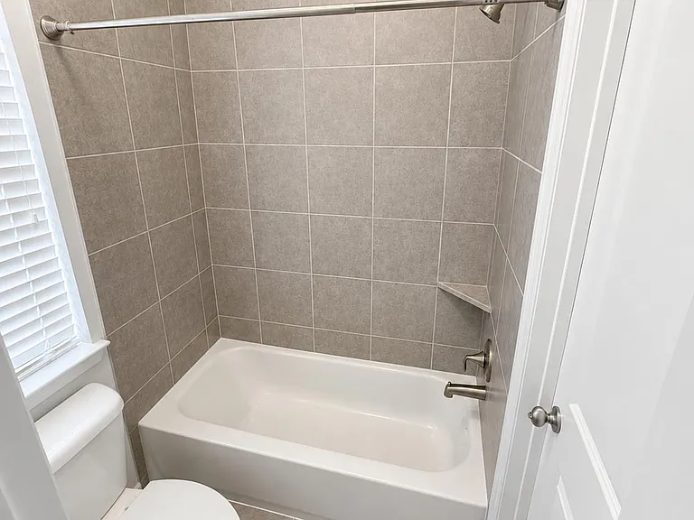 Full bathroom with a tiled tub/shower surround, shower rod, and a window for ventilation and natural light.