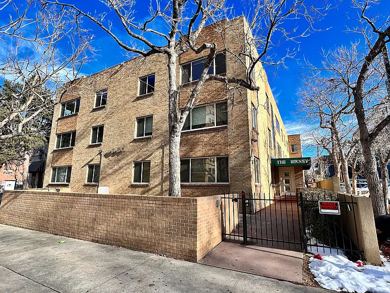 Charming brick apartment building under a vibrant blue sky, featuring gated entry and inviting surroundings at The Birney.