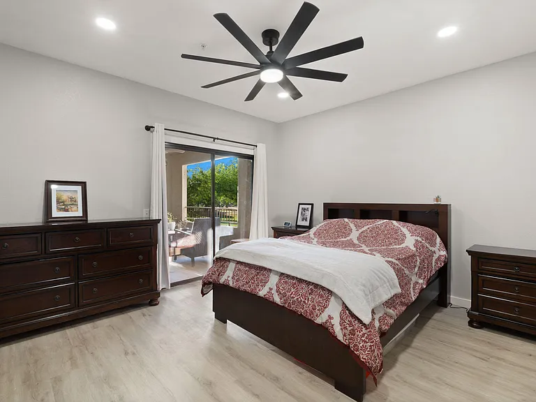 Spacious bedroom with a ceiling fan, large dresser, and sliding doors opening to a private patio for indoor-outdoor living.