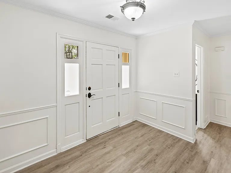 Grand entryway with decorative wainscoting, hardwood floors, and a welcoming front door with sidelights.