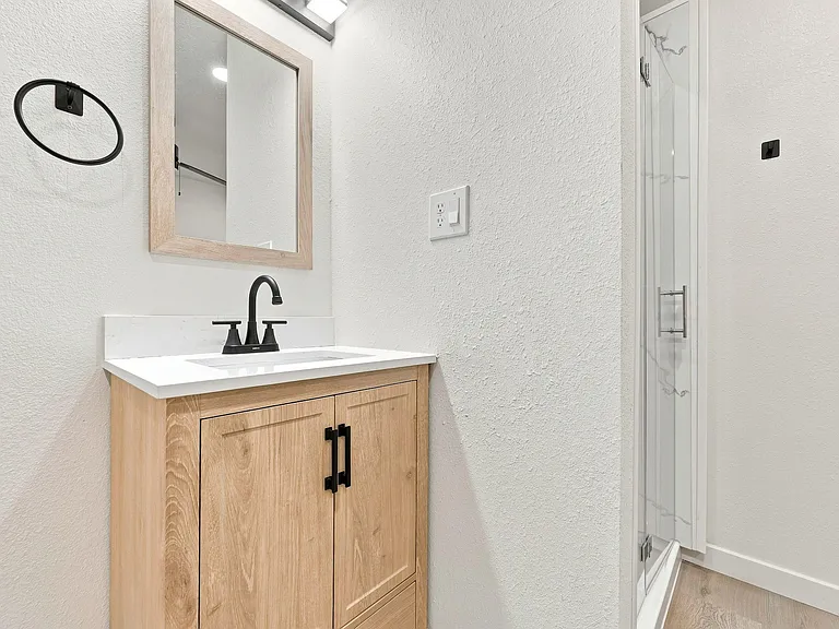 Updated bathroom vanity with quartz-style countertop, matte-black fixtures, and a glass-enclosed shower for easy daily use.