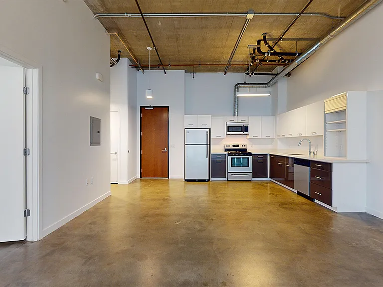 Apartment kitchen with stainless steel appliances, dining and living room with polished-concrete flooring.