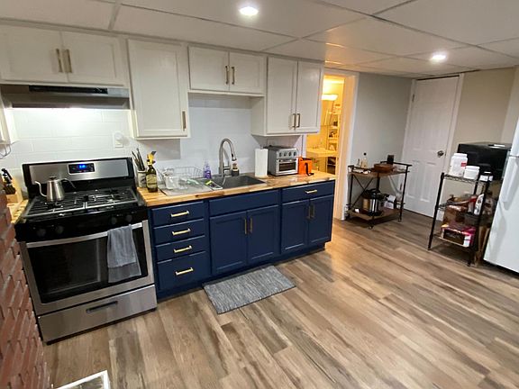 New kitchen with beautiful butcher block countertops, two tone cabinets with brass hardware, and stainless stove with vent.