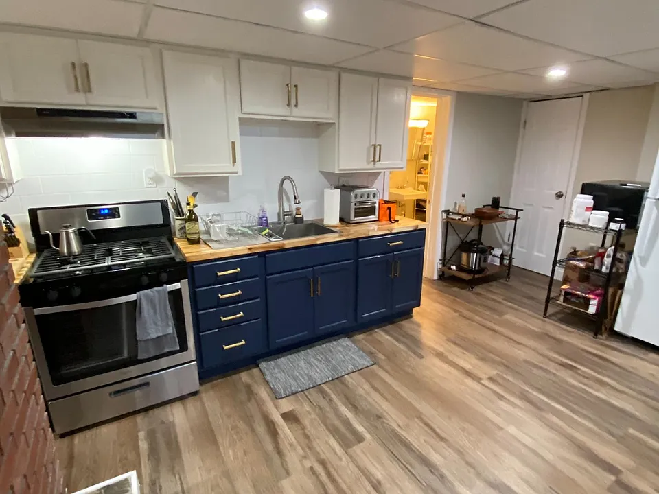New kitchen with beautiful butcher block countertops, two tone cabinets with brass hardware, and stainless stove with vent.