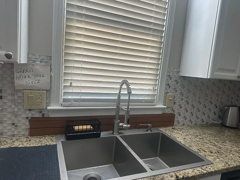 Kitchen sink area with a double-basin stainless sink, pull-down faucet, granite-look counters, and tiled backsplash.