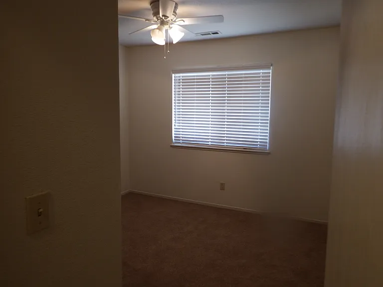 3rd bedroom with large window, wood blinds and ceiling fan.