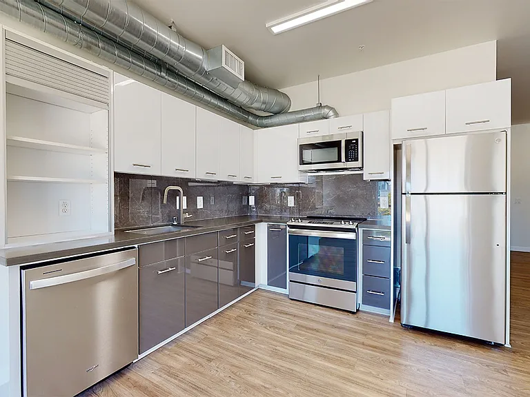 Apartment kitchen with stainless steel appliances, quartz countertops and wood-style flooring.
