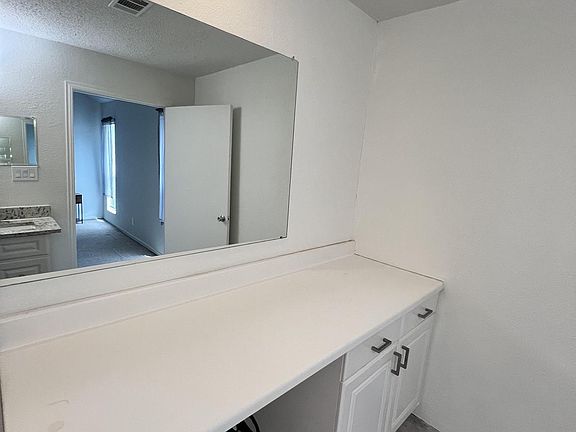 Bathroom vanity area with wide counter space, large wall mirror, and ample cabinet storage for daily essentials.